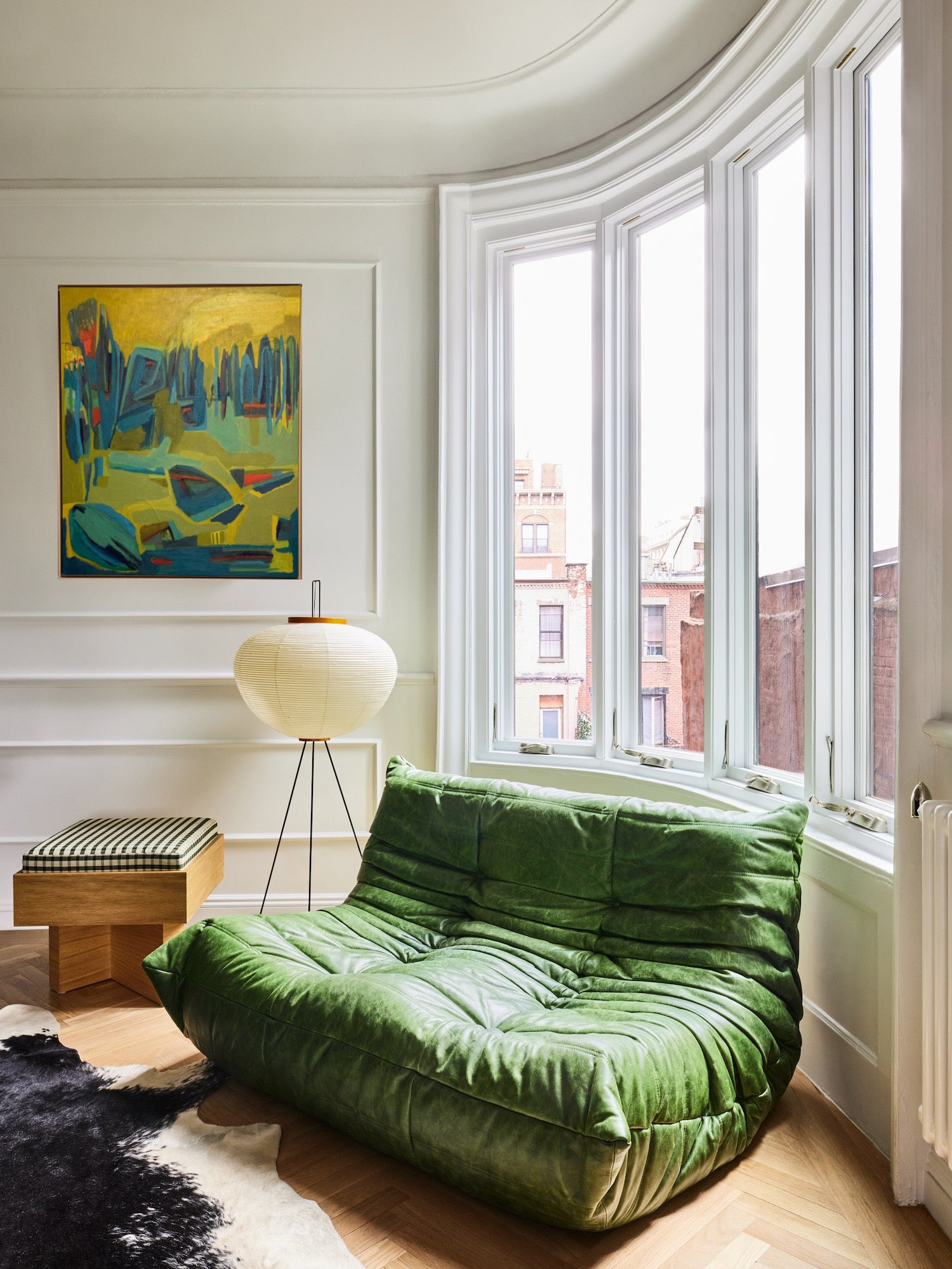 Green sofa in a room with large windows and original nature painting on the wall.