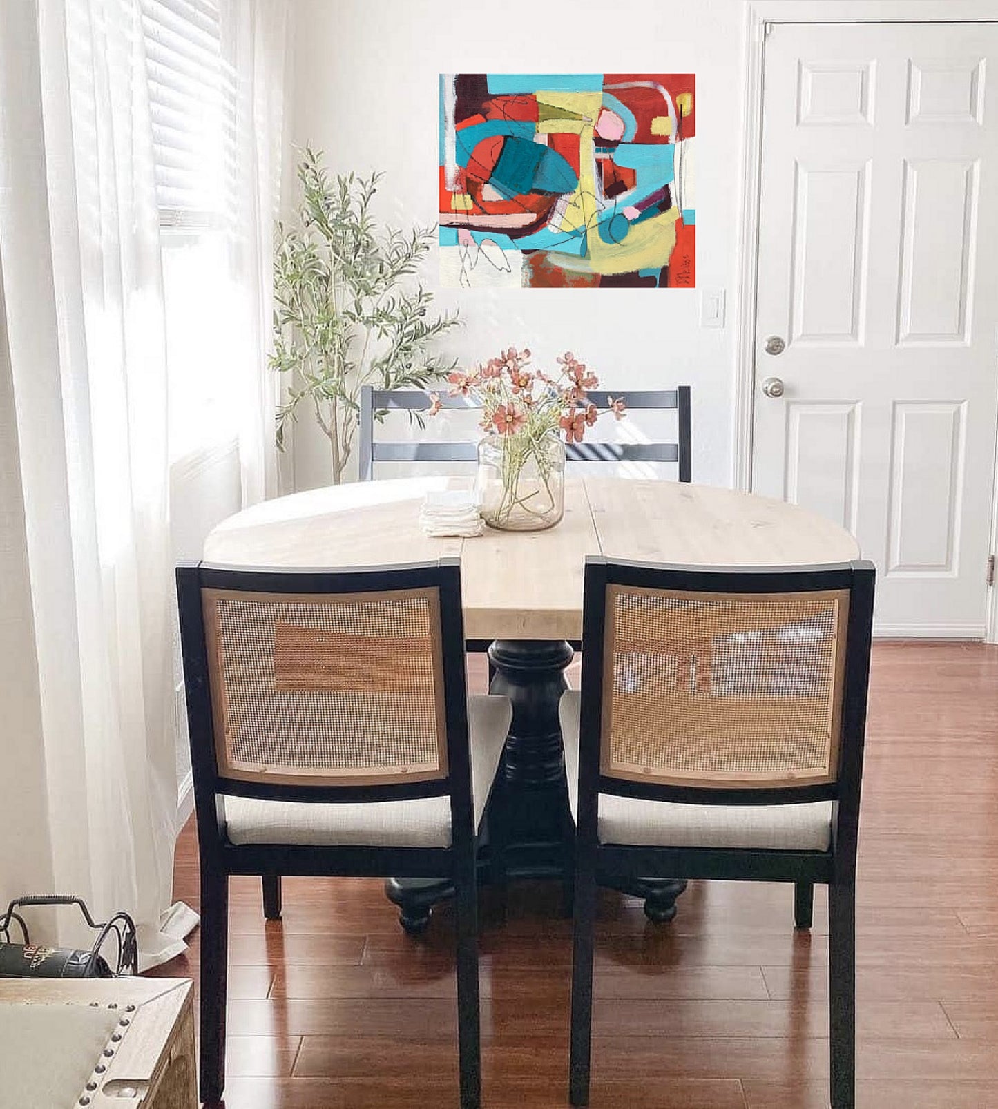 Red, yellow, aqua and white abstract painting on canvas created by artist danielle nelisse installed on white wall in modern dining room in front of contemporary dining set with vase of flowers on table