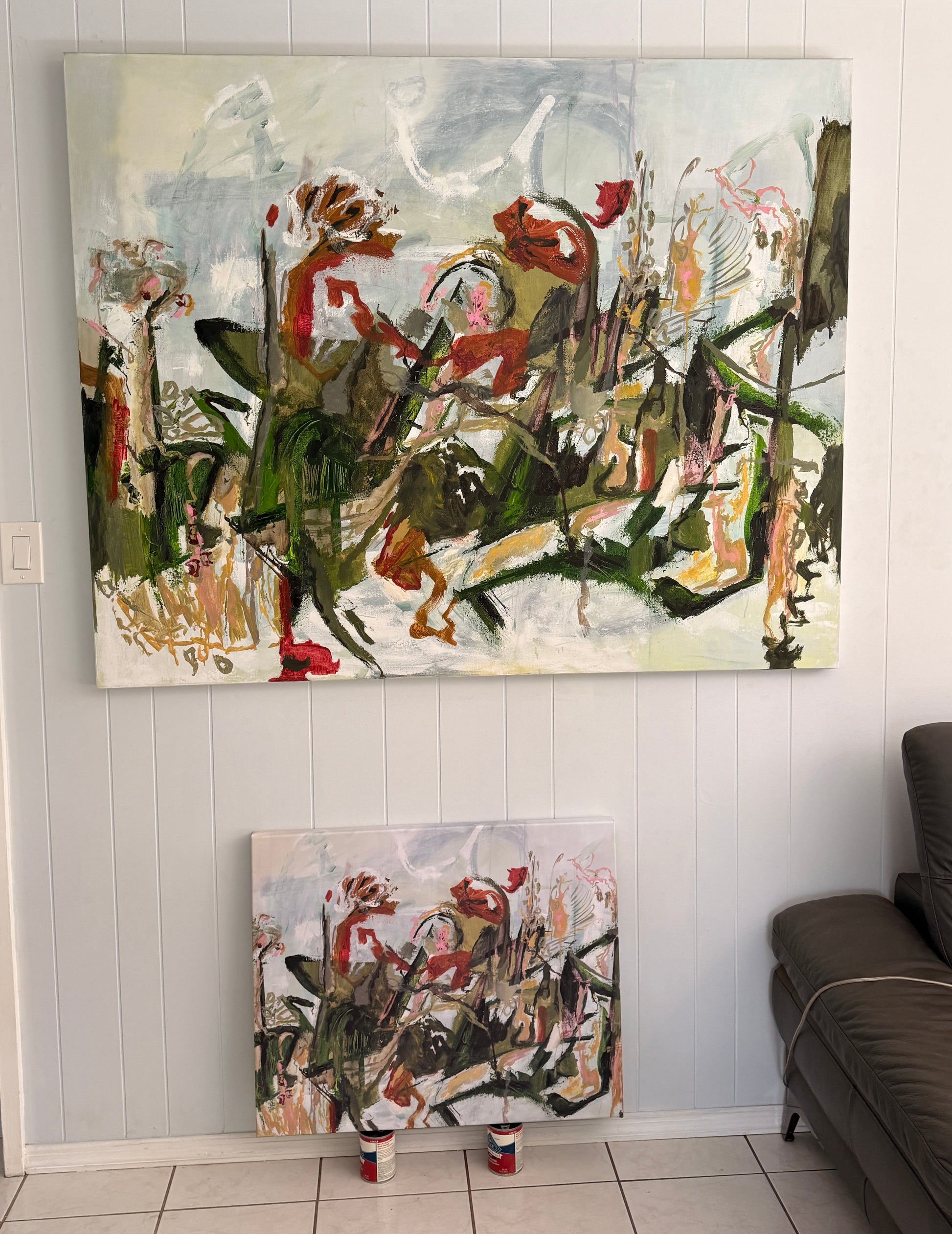 white coral and green abstract painting on a wall with a smaller version below it, in a room with a sofa.